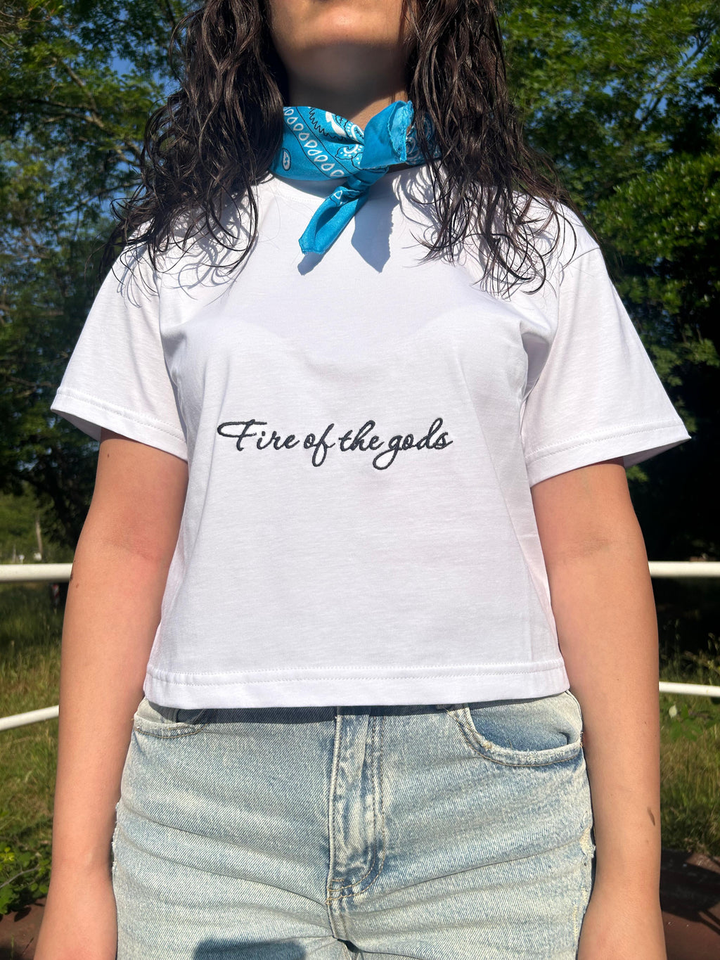 Ragazza con t-shirt bianca stampata Fire of the gods, bandana azzurra e shorts di jeans, outfit streetwear casual all'aperto.
