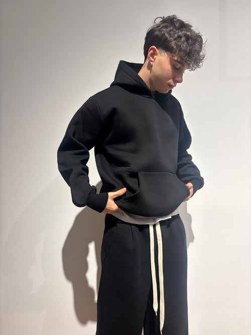 Giovane uomo con felpa nera con cappuccio e pantaloni streetwear, stile casual urbano