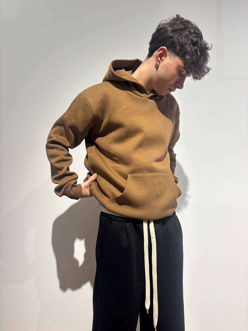 Modello indossa felpa marrone con cappuccio e pantaloni neri streetwear su sfondo neutro