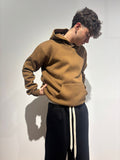 Modello indossa felpa marrone con cappuccio e pantaloni neri streetwear su sfondo neutro