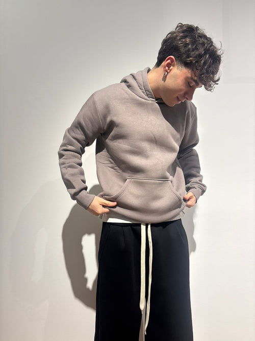 Ragazzo con felpa cappuccio grigia e pantaloni neri stile streetwear, sfondo neutro