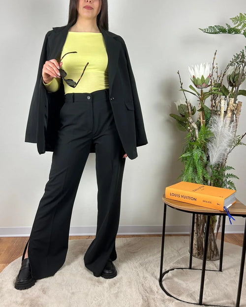 Donna indossa outfit streetwear: blazer nero, maglia gialla, pantaloni neri, mocassini, occhiali da sole